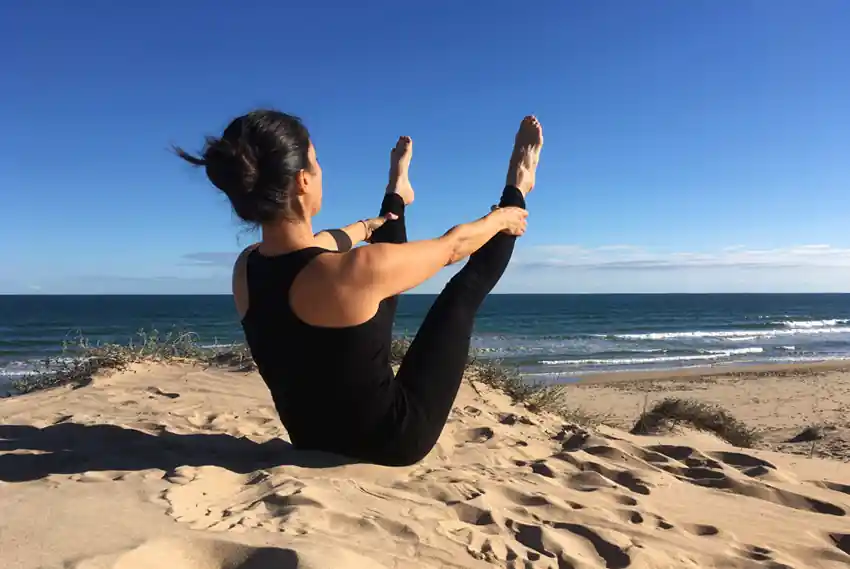 Fátima Pastor haciendo el ejercicio de Pilates La Hamaca en una duna con el mar de fondo
