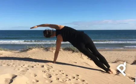 Fátima Pastor haciendo un ejercicio de Pilates Mat en una duna con el mar de fondo
