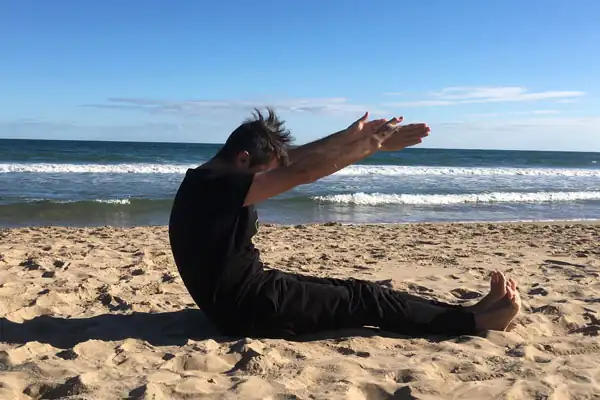 Vicente Juan Asencio ejecutando ejercicio de Pilates Roll Up en la playa