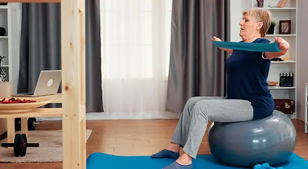 Mujer madura realizando un ejercicio de Pilates Mat con banda elástica sobre fitball
